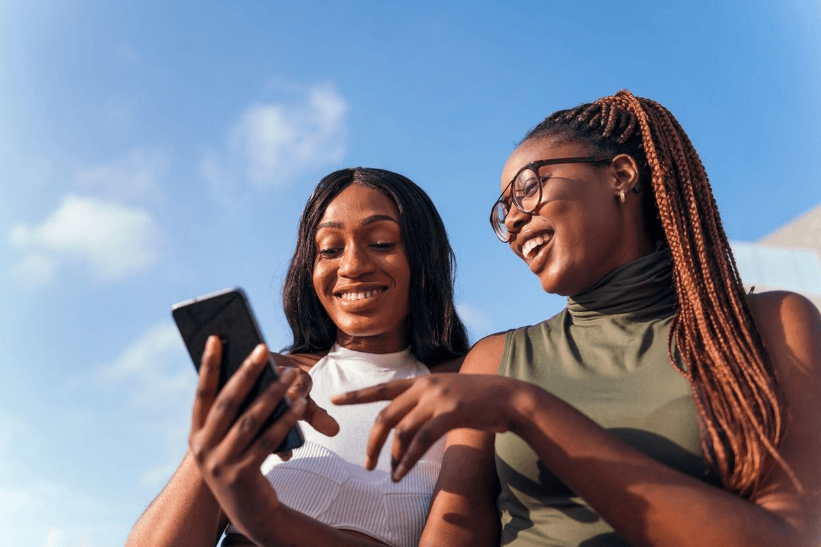 Two friends smiling at a phone outdoors
